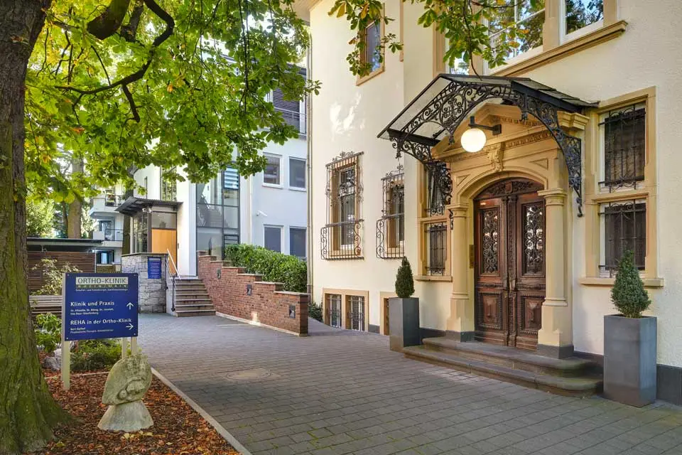Eingangsbereich der Ortho-Klinik Rhein-Main mit historischer Holztür und schmiedeeisernem Vordach
